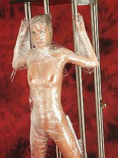 Full body plastic wrapping: teenage beauty is nude and bound spread with lots of tape