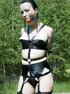 Young lady is taken for a stroll dressed in black lingerie, bound with BDSM harness and ball gagged