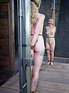 A couple of naked blondes are looking at each-other chained and bound with steel restraints