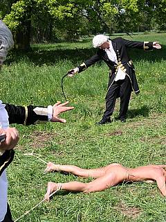 Blonde is helplessly spread-eagled on the grass and whipped by a couple of men in costumes and wigs