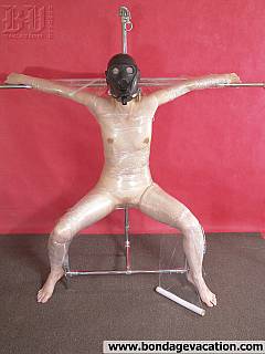 Nude slut is wearing gas mask, collared and crucified with plastic tape bondage