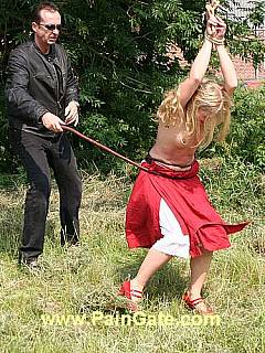Topless blond is tied by her wrists and there is thick bull whip is wrapping around her waist within each painful lash