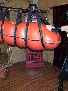 Woman is enjoying the feeling of complete helplessness when put into inflatable rubber cocoon and then suspended on belts