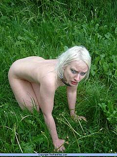 Chained blond is fully nude and crawling in the grass while BDSM master is canning her with a stick