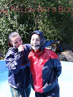 A couple of girls are both dressed up in nylon rain-wear and having fun in the pool with their hands tied behind the back