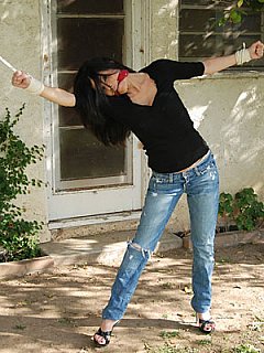 Woman tied spread outdoors, gagged with scarf and stripped