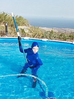 Girl is cleaning the pool while wearing blue rubber ourfit and a gas mask