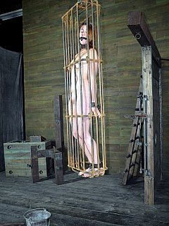 Naked woman is put in a cage, suspended and then her feet are being tortured with open flames