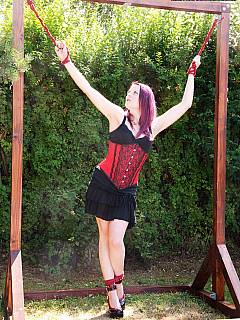 One sexy redhead is tied spresd eagle outdoors by another