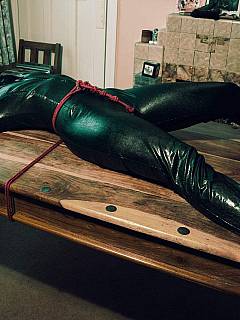 MILF in a black catsuit is tied to table and gagged with scarf