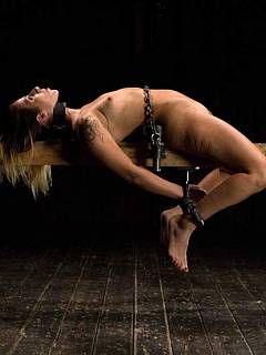 Shaved bondage girl is restrained with leather belts and having her legs spread wide