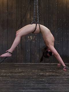 Steel restraints are holding the girl motionless while two guys are penetrating her with their fingers and sticks