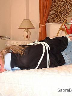 Hogtied woman is resting on the bed fully dressed