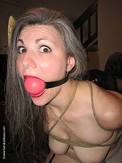 Bandaged wife is sitting on the chair enjoying an extremely big ball gag in her mouth