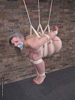 Ball-tied woman is hanging up in the air like a fruit: totally naked and gagged with duct tape