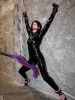 Catwoman in captivity: woman is black PVC suit is spread-eagled along the wall and whipped