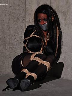 Black babe is dressed up in business suit and posing in bondage on the concrete floor